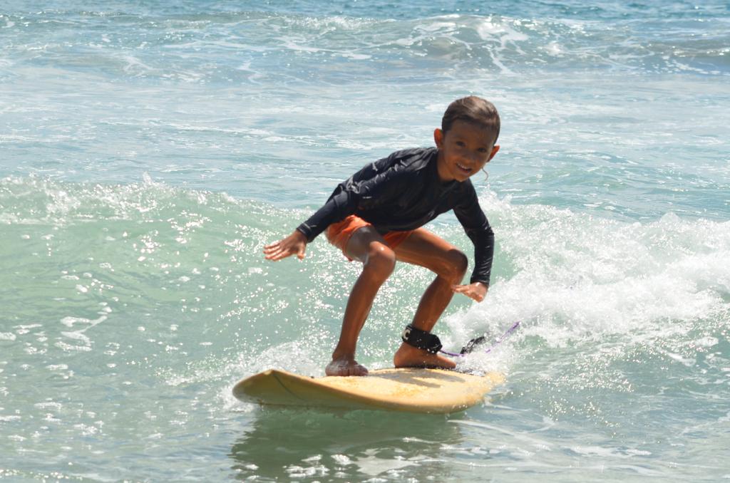 Young child smiling while surfing a wave on a yellow soft-top board during a surf lesson in Manuel Antonio, Costa Rica